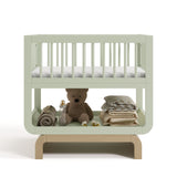 Santorini sage with driftwood bassinet front view with baby items on bottom shelf
