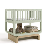 Santorini sage with driftwood bassinet angle view with baby items on bottom shelf