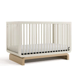 Baby crib in two-tone colorway, at an angled view (Frosted Oat with Driftwood)