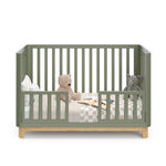 Front view of an olive crib with a natural wood color base, featuring guard rails in toddler bed conversion