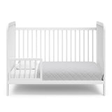 White crib in toddler bed conversion with one safety guardrail