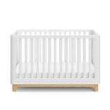 Front view of a white crib with a natural wood color base