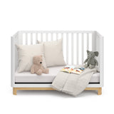 Front view of a white crib with a natural wood color base in daybed conversion